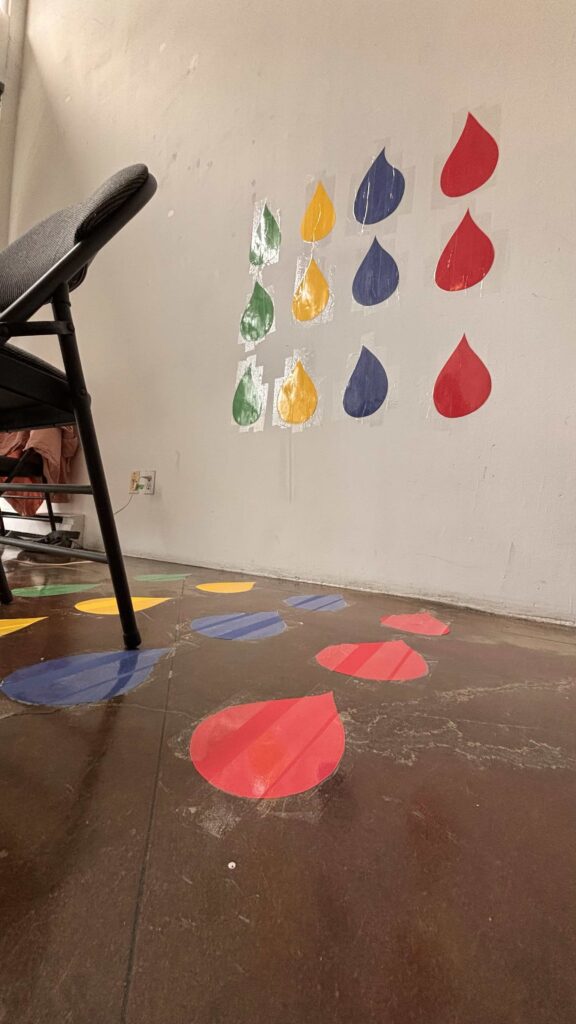 A grid of coloured droplet shapes stuck on the wall and floor in a grid layout.